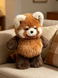 A plush red panda stuffed animal sitting on a beige sofa in a softly lit indoor setting.